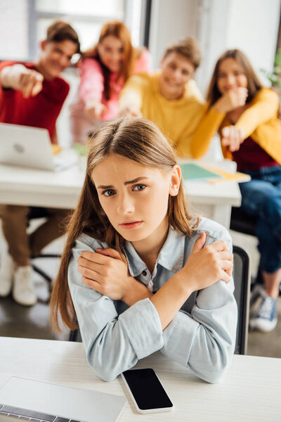schoolchildren laughing while bullying sad girl on foreground