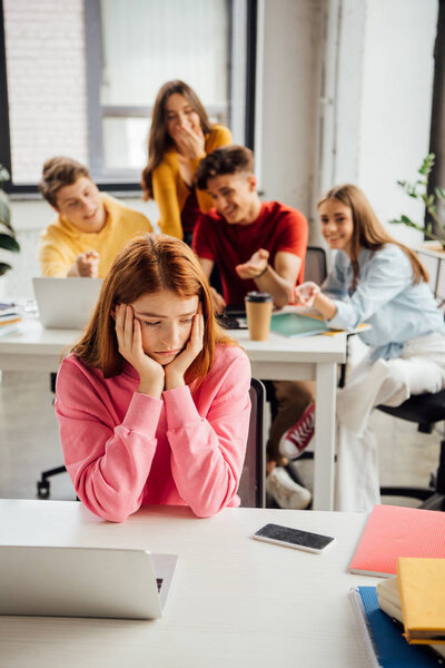 schoolchildren laughing while bullying sad girl on foreground