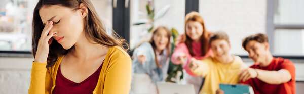 panoramic shot of sad girl and laughing schoolchildren pointing with fingers at her
