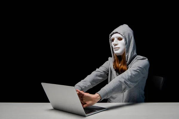 黒で隔離されたサイバーいじめの間にラップトップの近くに座って 手を伸ばすマスクとパーカーの匿名の女の子 — ストック写真