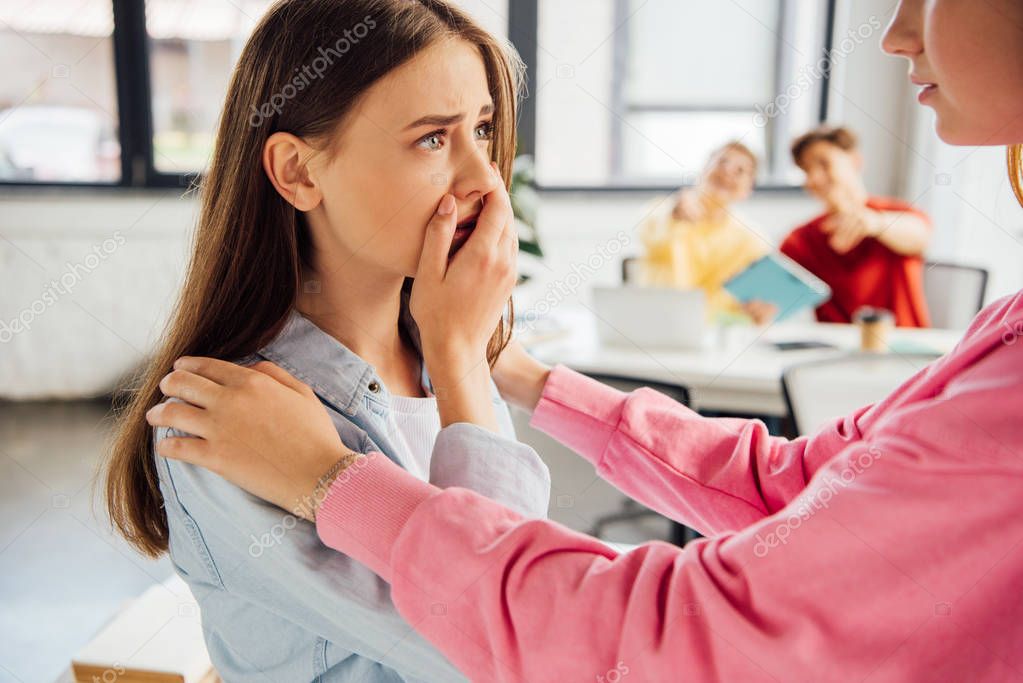 partial view of girl supporting sad friend in school