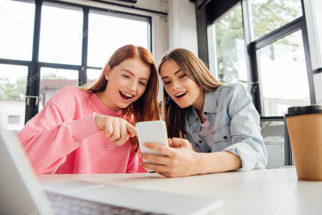 two excited girls smiling while using smartphone in school