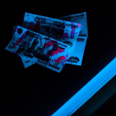 selective focus of blue ultraviolet lightning on russian money on black  clipart