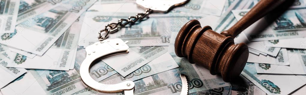 panoramic shot of wooden gavel near handcuffs on russian money 