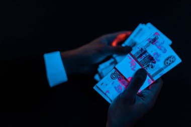cropped view of man holding russian money under blue uv lighting isolated on black  clipart