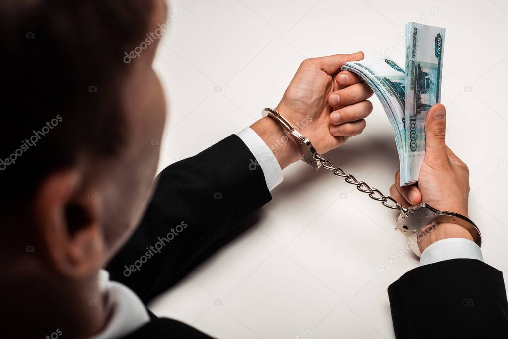 selective focus of businessman in handcuffs holding bribe on white 