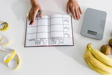 defter ve meyvelerin yanında kalem tutan kadının kırpılmış görünümü 
