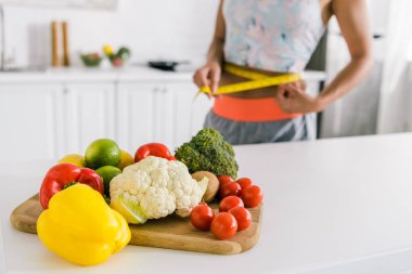 selective focus of vegetables on cutting board near woman measuring waist  clipart