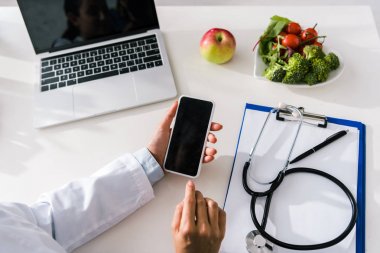 dizüstü bilgisayar ve pano yakınında boş ekran ile akıllı telefon tutan doktor havai görünümü 