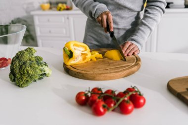 selective focus of woman cutting yellow paprika near cherry tomatoes and broccoli  clipart