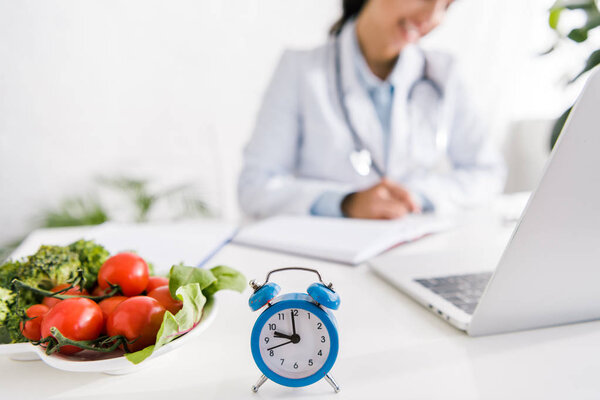 cropped view of nutritionist near vegetables and alarm clock 