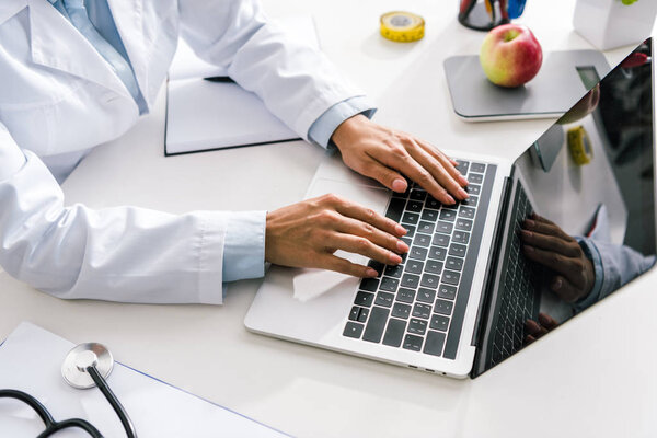 cropped view of doctor typing on laptop with blank screen 