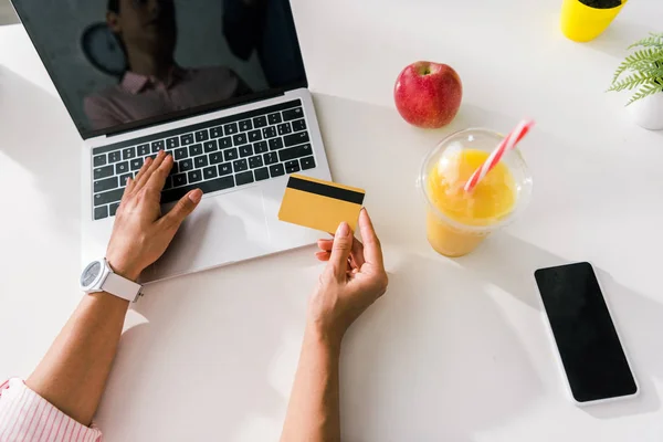 overhead view of girl holding credit card near laptop and smartphone with blank screens