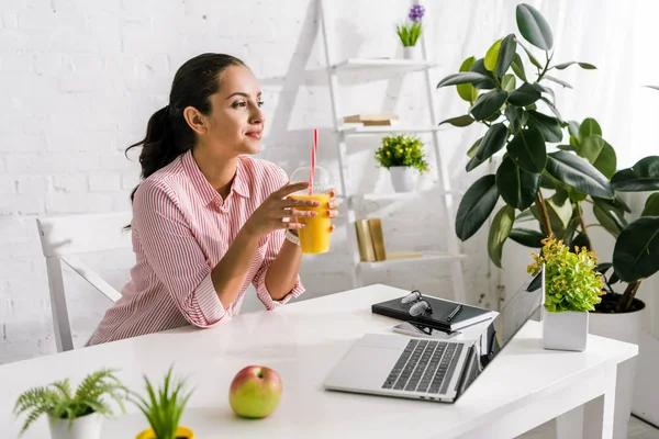 Wanita Ceria Memegang Cangkir Plastik Dengan Jus Jeruk Dekat Laptop — Stok Foto