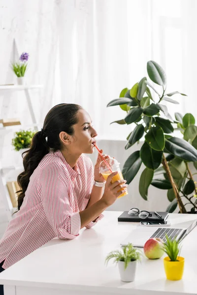 有吸引力的女孩喝橙汁附近的笔记本电脑 — 图库照片