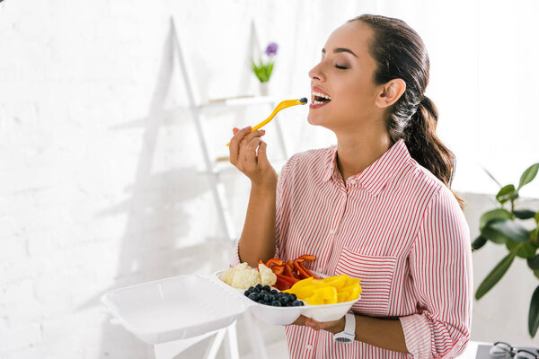 happy girl with closed eyes eating blueberry 