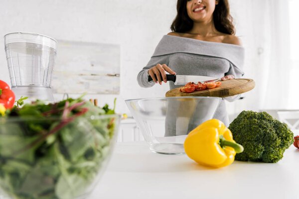 selective focus of happy woman holding cutting board with red cherry tomatoes 