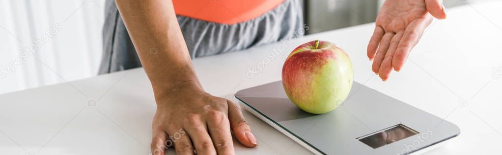 panoramic shot of woman gesturing near food scales and apple 