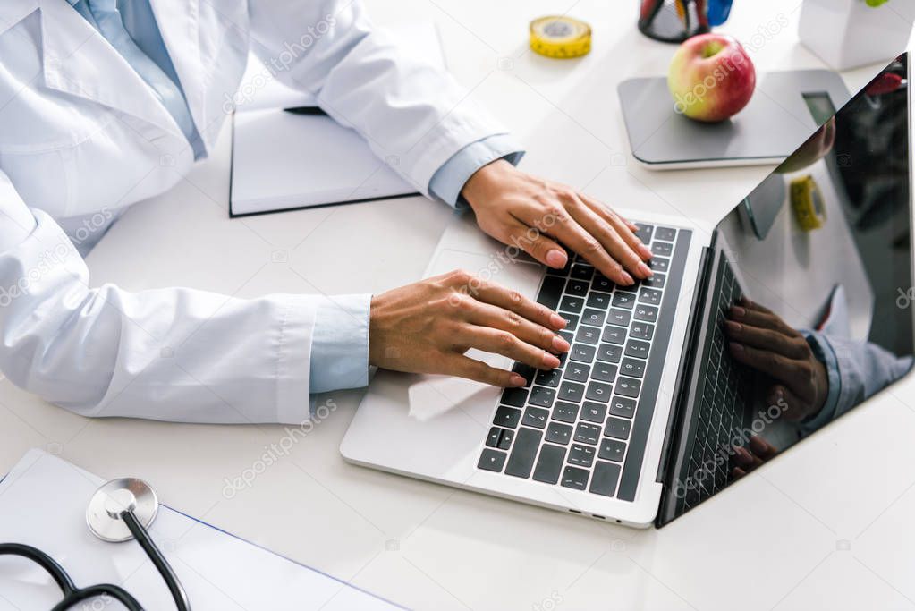 cropped view of doctor typing on laptop with blank screen 