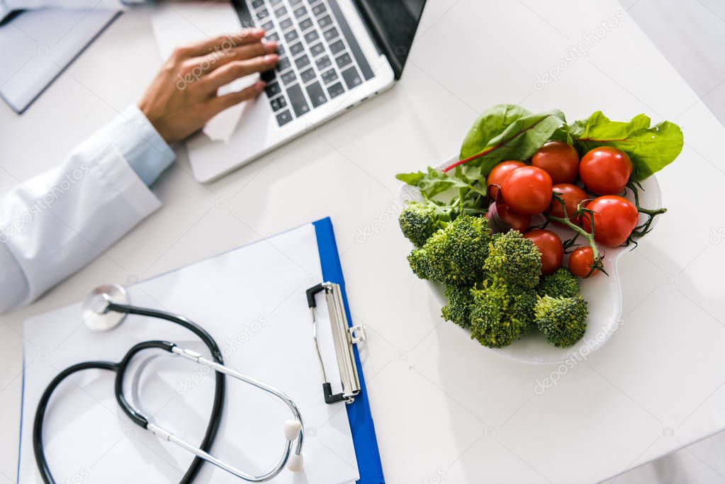 selective focus of vegetables near doctor typing on laptop 