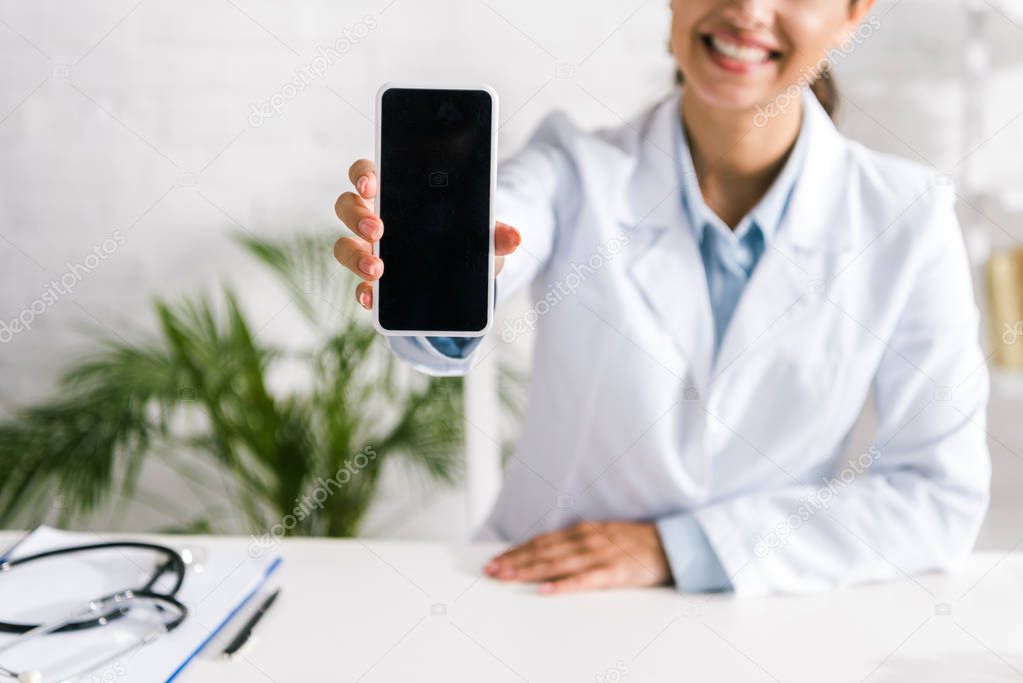 cropped view of happy doctor holding smartphone with blank screen 