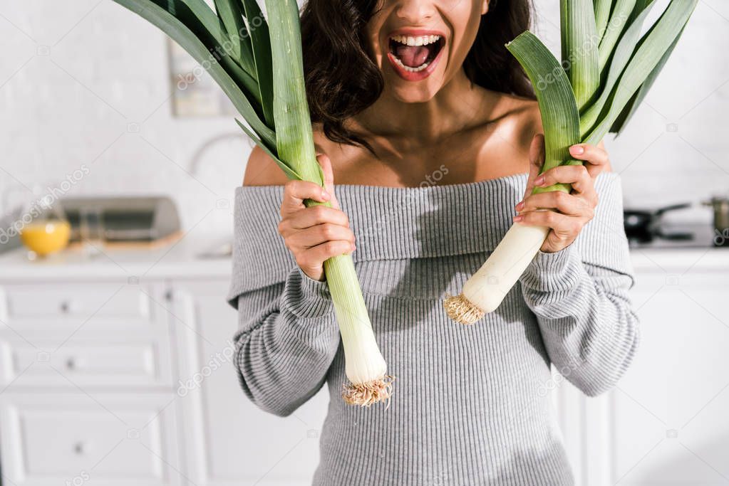 cropped view of excited woman holding leek in kitchen 