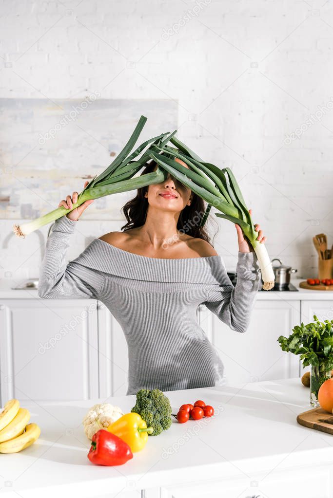 attractive girl holding leek near face and tasty vegetables on table 