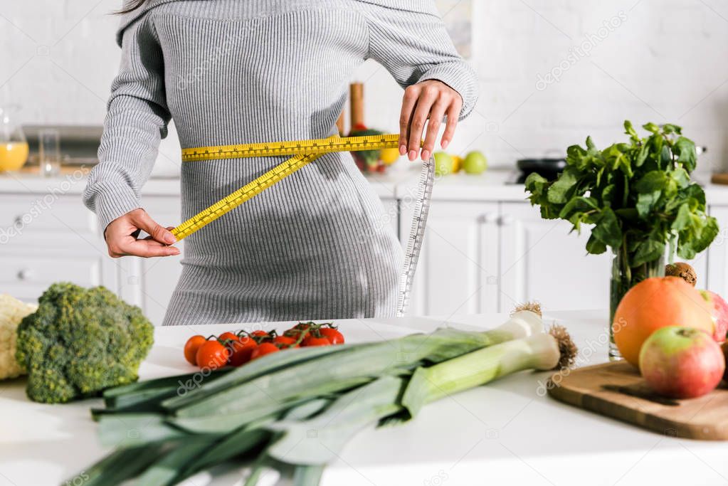 cropped view of woman measuring waist near vegetables on table 