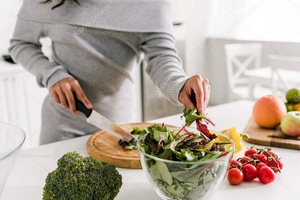 cropped view of woman holding knife near broccoli and paprika 