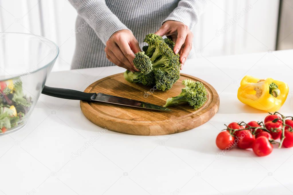 cropped view of woman holding green broccoli near bowl and fresh vegetables 