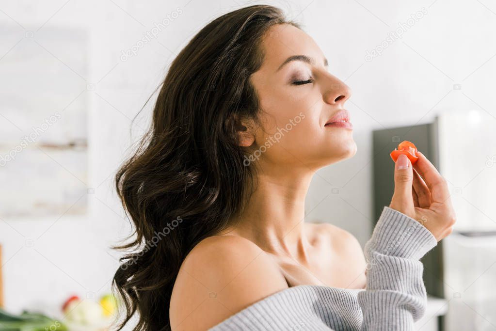 attractive girl with closed eyes holding red cherry tomato 