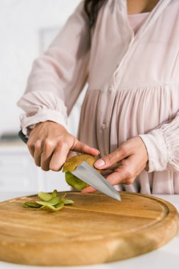 cropped view of pregnant woman peeling tasty ripe kiwi  clipart