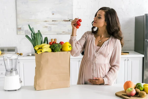 紙袋の近くでチェリートマトを見て幸せな妊娠中の女性 — ストック写真