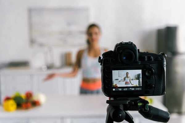 selective focus of digital camera with woman gesturing near vegetables on screen 