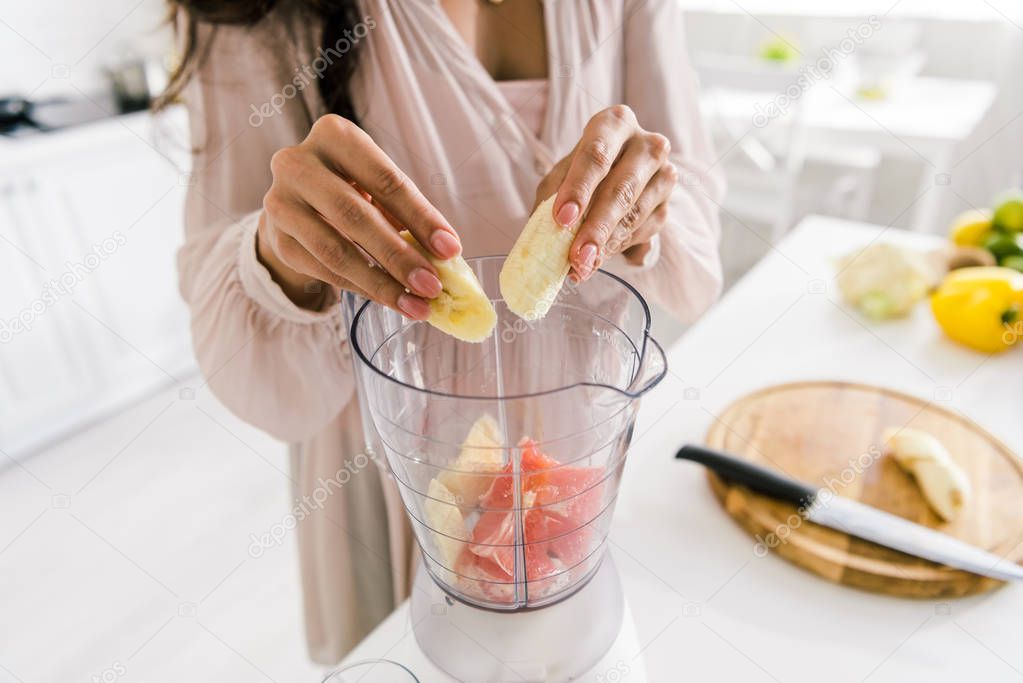 cropped view of pregnant woman putting banana in blender with grapefruit 