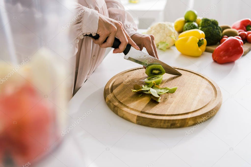 selective focus of pregnant woman cutting kiwi on chopping board 