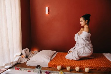spa salonunda masaj mat üzerinde oturan bornoz çekici kadın