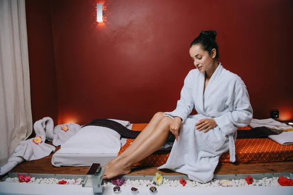 spa salonunda masaj mat üzerinde oturan bornoz çekici kadın