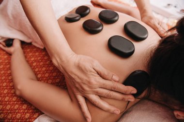 spa salonunda kadına sıcak taş masajı yapan masör kırpılmış görünümü 