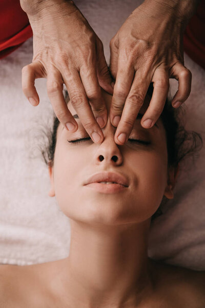 cropped view of masseur doing face massage to woman in spa salon 