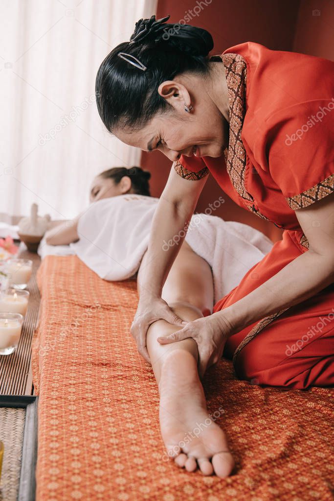 selective focus of asian masseur doing foot massage to woman in spa salon 