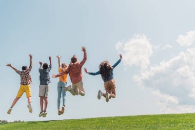 mavi gökyüzüne karşı atlama ve gesturing çok kültürlü çocukların geri görünümü 