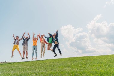 neşeli çok kültürlü çocuklar atlama ve mavi gökyüzüne karşı gesturing 