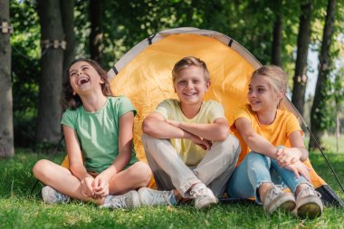 happy boy sitting with cute friends laughing near camp  clipart