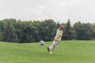 parkta yeşil çim üzerinde futbol oynayan sevimli çocuk 