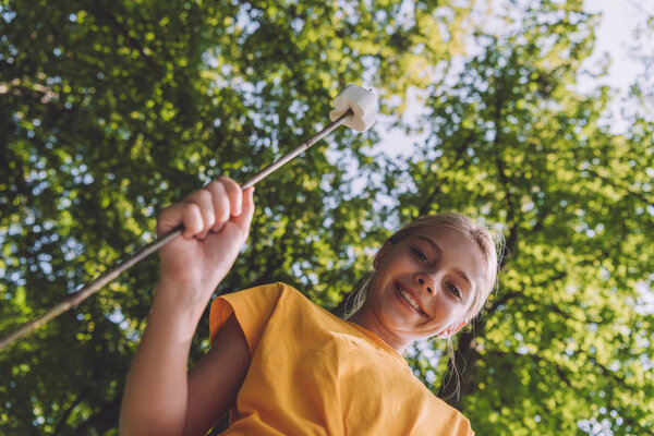 low angle view of happy kid holding sweet marshmallow on stick 