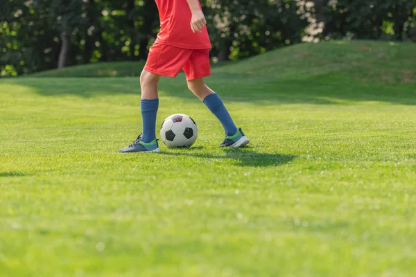 selective focus of kid in red sportswear playing football 