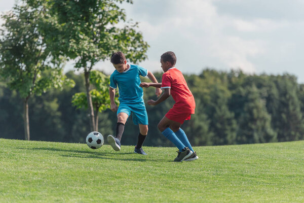 милые мультикультурные дети играют в футбол на траве
 
