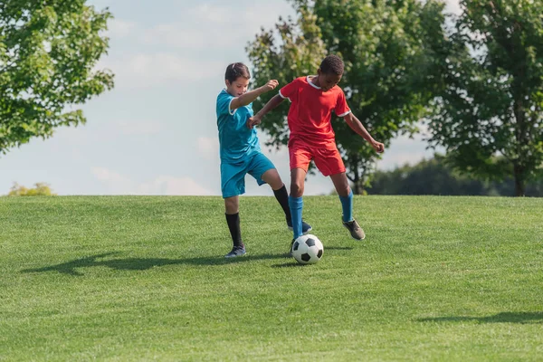 adorable multicultural children playing football on grass 