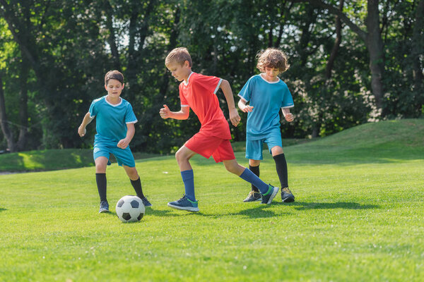 cute friends in sportswear playing football on green grass in park 